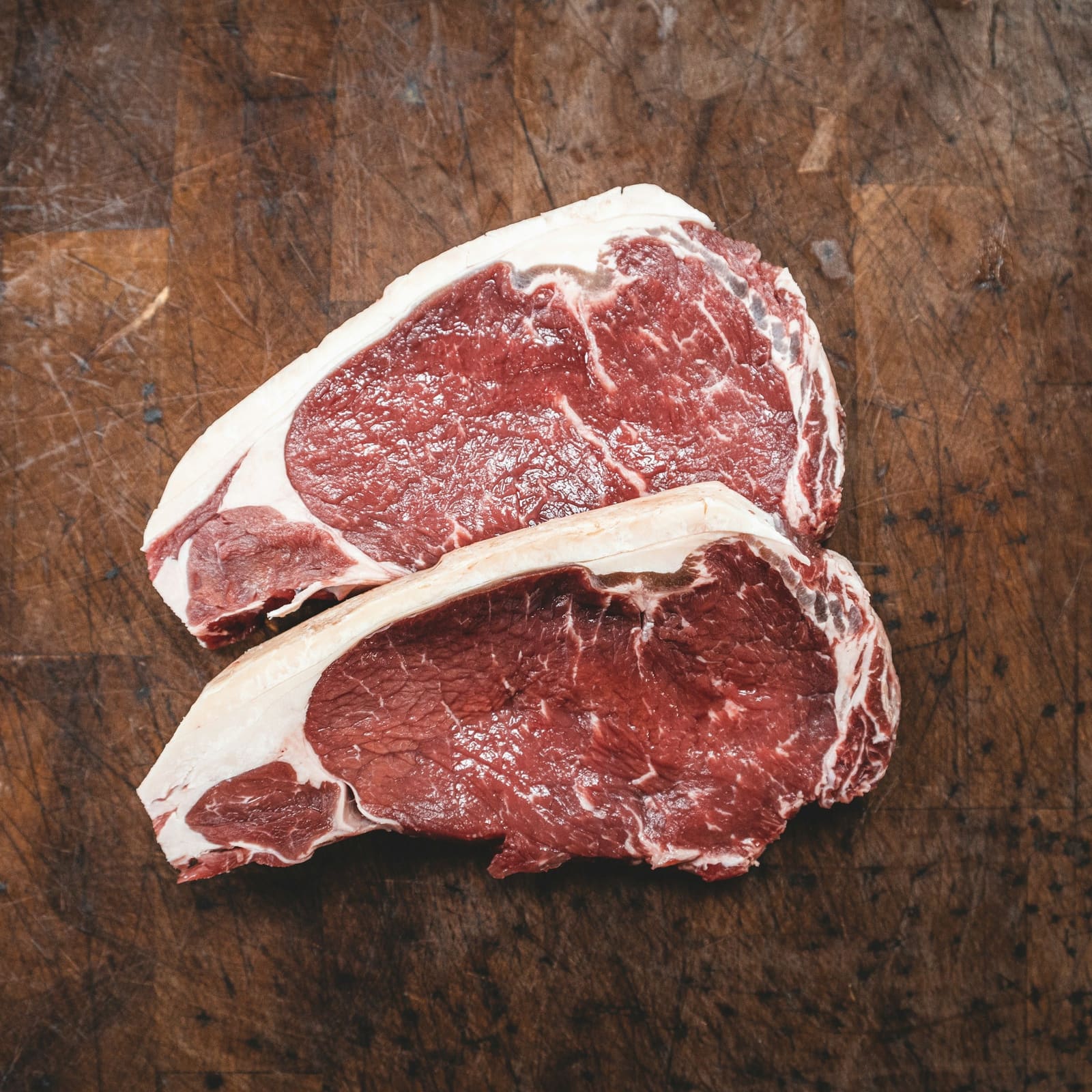 Two raw steaks on a wooden butcher block